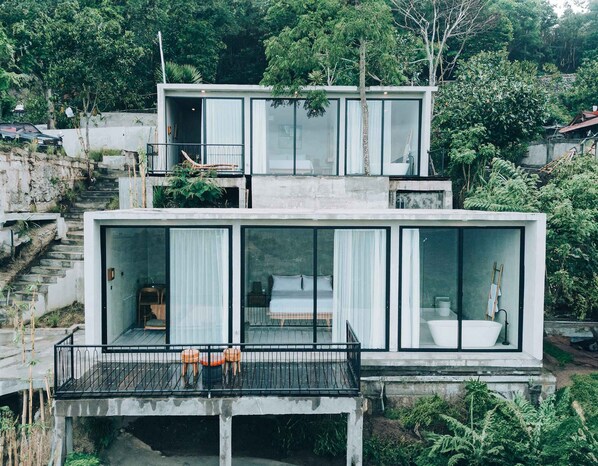 Una casa moderna de dos pisos con amplios ventanales, un balcón con asientos y una escalera que conduce al nivel superior.