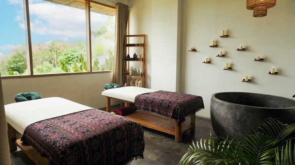 A room with two beds, a large stone tub, and a shelf with bottles.