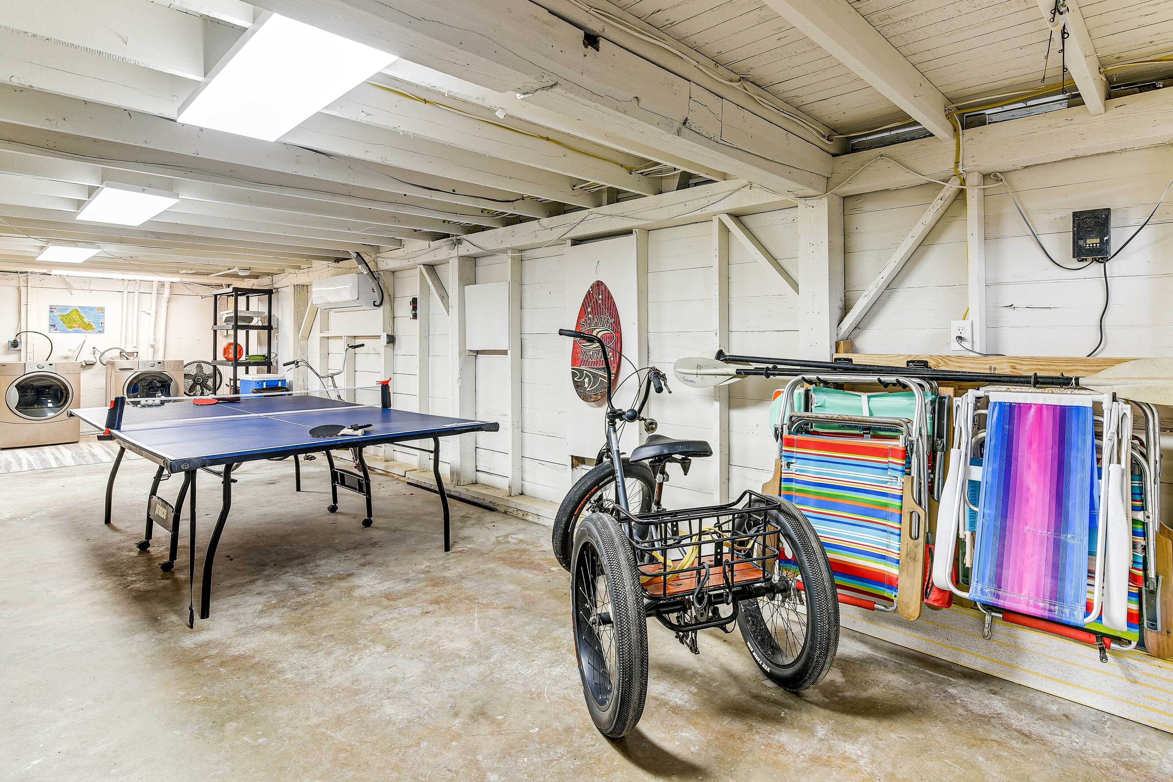 En rummelig stue med et ping pong bord, en cykel med kurv, og farverige håndklæder hængende på væggen.