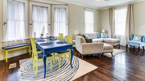 A spacious living room with a dining area, featuring a blue table and yellow chairs, a beige sofa, and a blue ottoman. - Walk to Beach! Family-friendly Galveston Home (Galveston)
