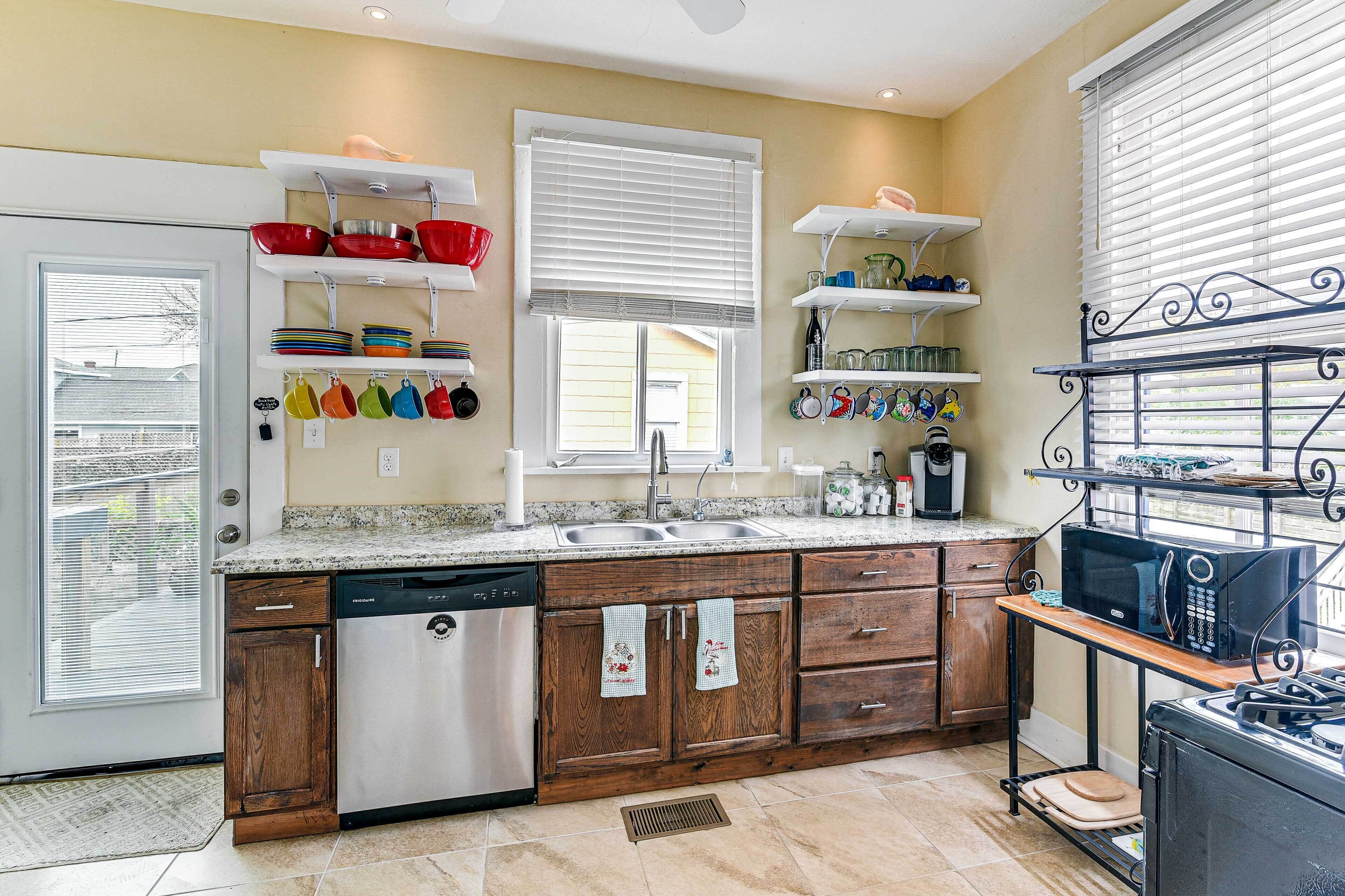 A kitchen with wooden cabinets, a dishwasher, a sink, and a microwave. There are shelves with dishes and a window with blinds.