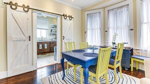 A dining area with a blue table and yellow chairs, a kitchen in the background, and a sliding barn-style door. - Walk to Beach! Family-friendly Galveston Home (Galveston)
