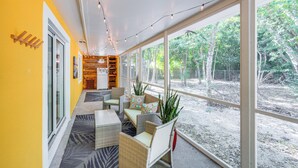 A bright, sunlit room with large windows, wicker furniture, and a view of trees outside. - Walk to Harry Harris Beach: Modern Coastal Escape! (Tavernier)