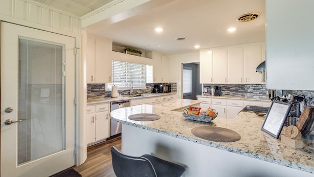 A modern kitchen with white cabinetry, a granite countertop, and a breakfast bar. - Home w/ Patio & Games Near Dtwn Pensacola! (Pensacola)