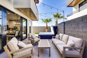 Une terrasse extérieure avec un canapé, des fauteuils, une table et un jacuzzi.