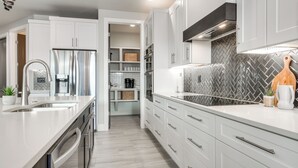 Une cuisine moderne avec des meubles blancs, des appareils en acier inoxydable et un dosseret de carrelage disposé en motif chevron.