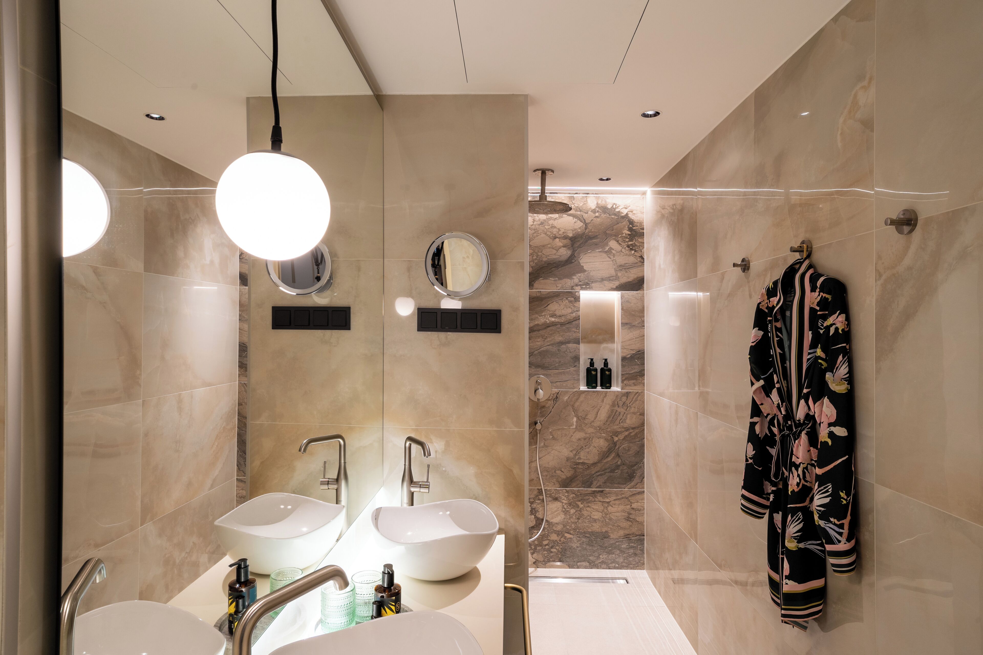 A modern bathroom with two sinks, a large mirror, and a robe hanging on the wall.