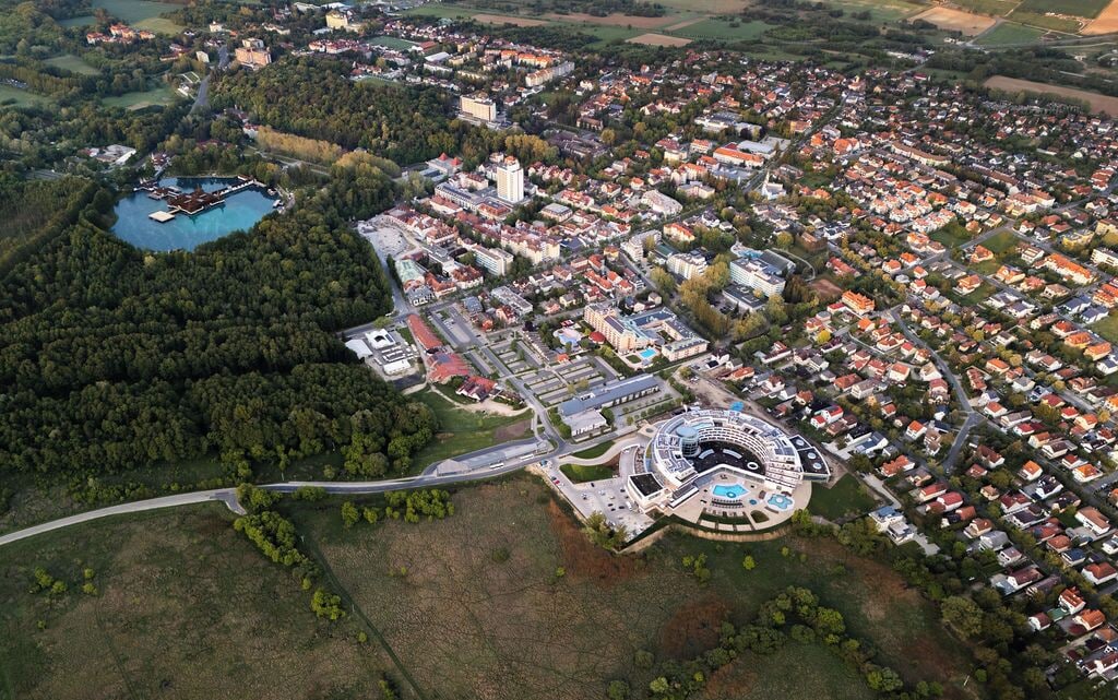 An aerial view of a town with a central round building, surrounded by residential areas and a lake.