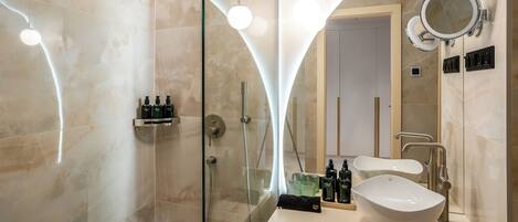 Un baño moderno con ducha envuelta en vidrio, tocador con un espejo grande y lavamanos.