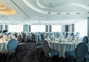 Un amplio salón de banquetes con mesas redondas dispuestas para comer, con sillas modernas y manteles blancos.