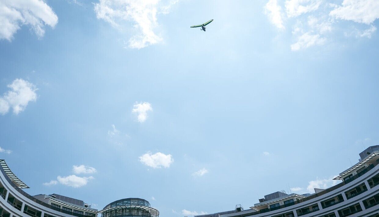 Ein modernes Gebäude mit einer geschwungenen Glasfassade und einem klaren Himmel, an dem ein Flugzeug vorbeifliegt.