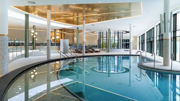 Una piscina interior con diseño moderno, rodeada de zonas de descanso y amplias ventanas.