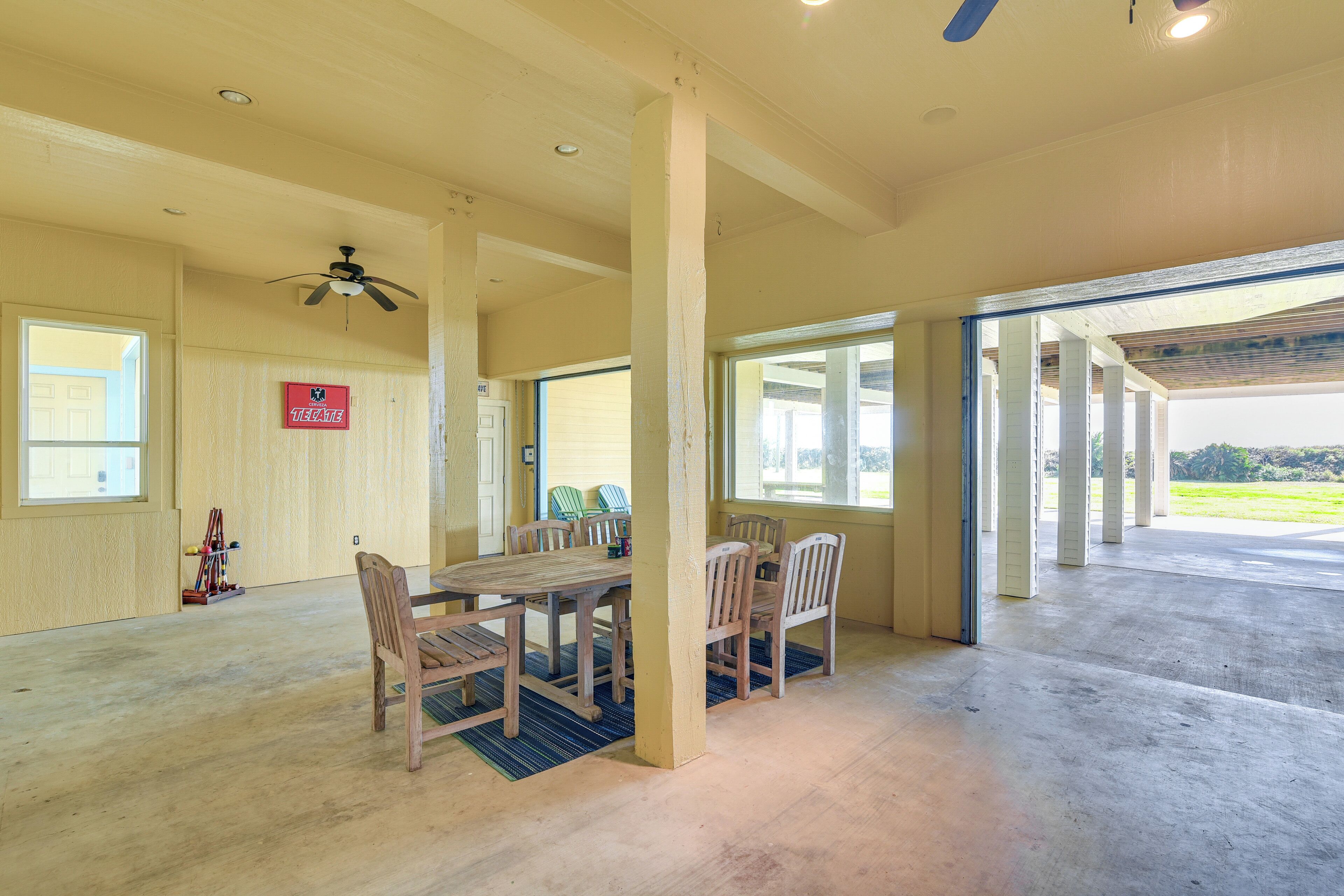 A spacious room with a wooden dining table and chairs, a ceiling fan, and large windows.