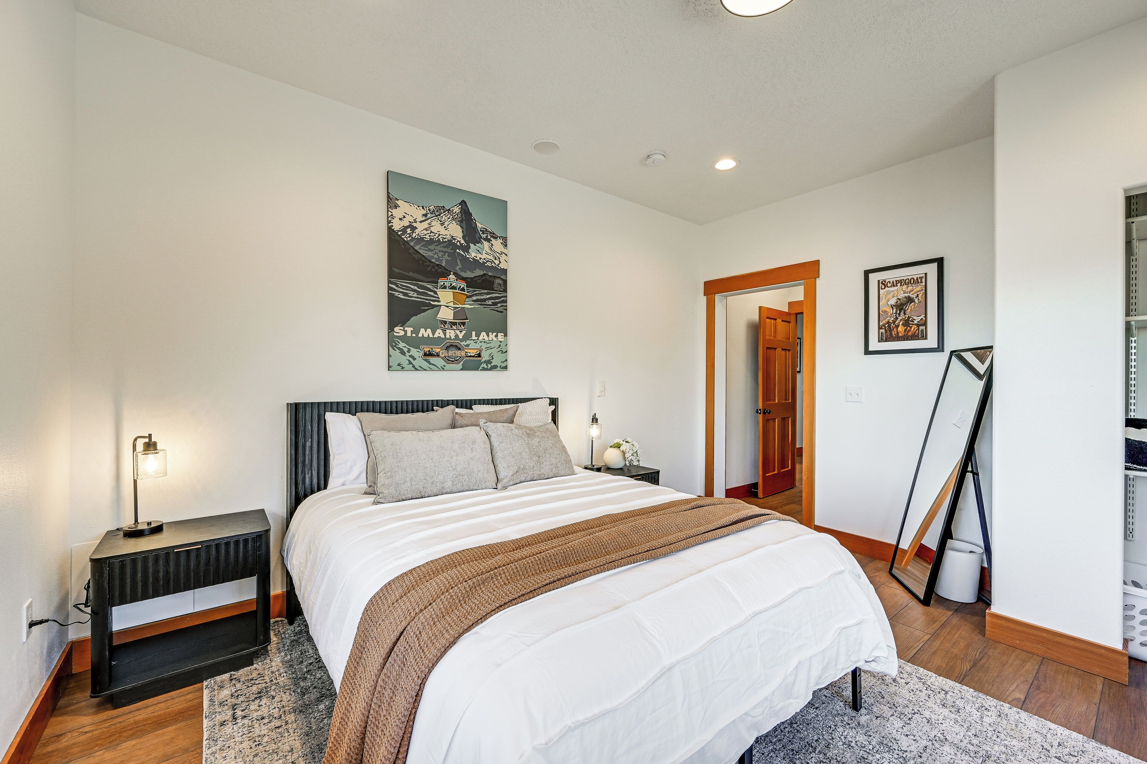 A bedroom with a bed, a nightstand, a lamp, a poster on the wall, and a door leading to another room.