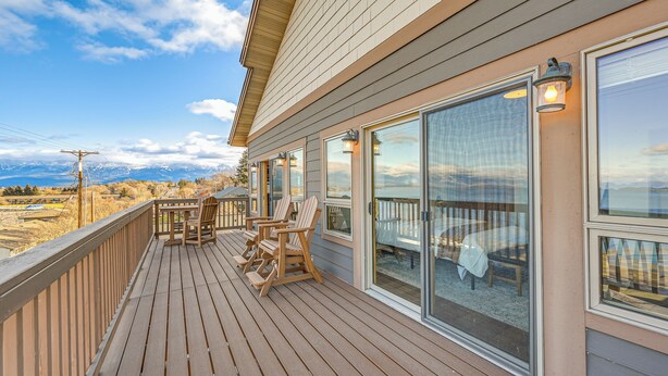 Une terrasse en bois, dotée de mobilier d’extérieur, de grandes fenêtres et offrant une vue sur les montagnes.