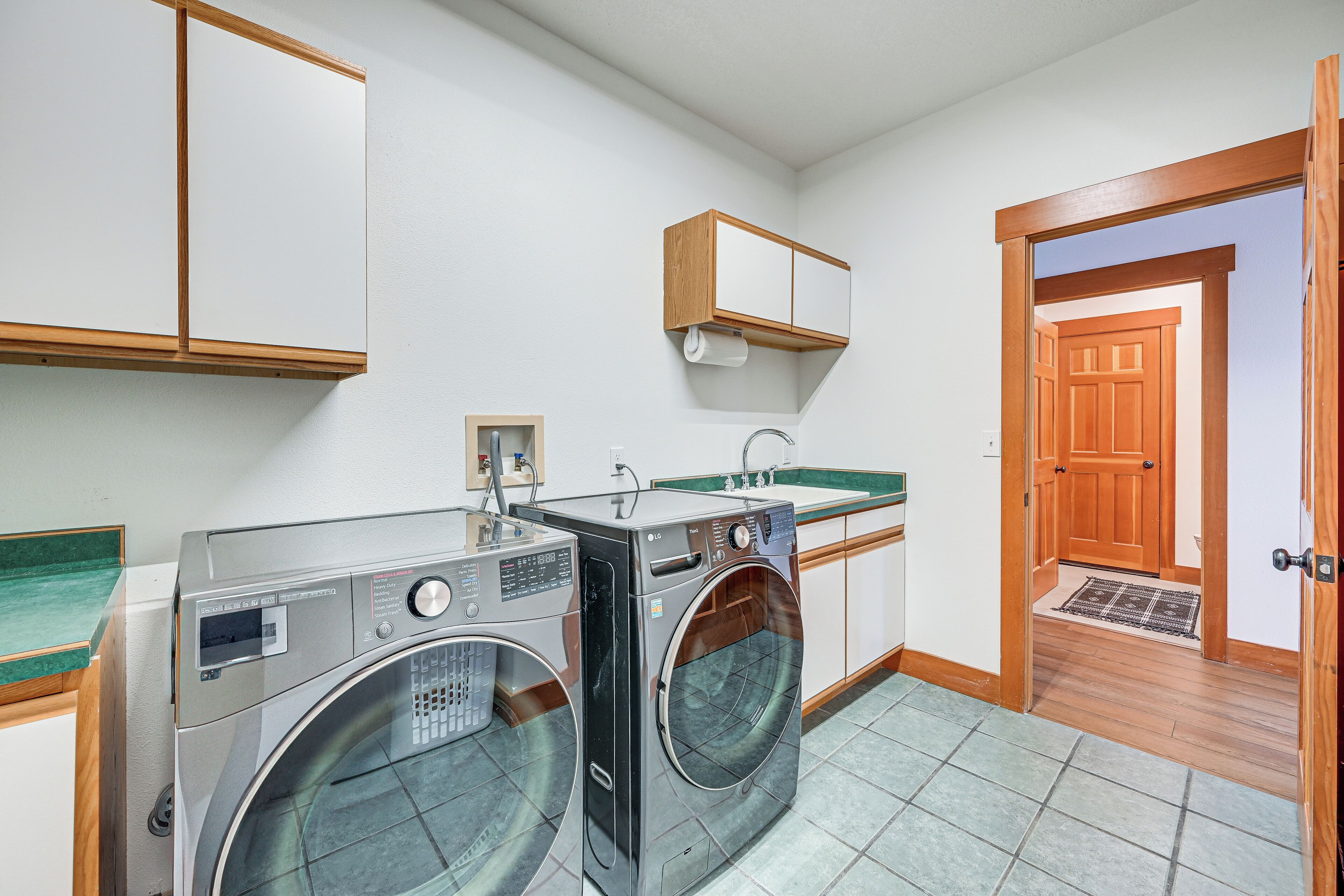 A laundry room with two front-loading washing machines, a wooden cabinet above the machines, and a wooden door leading to another room.
