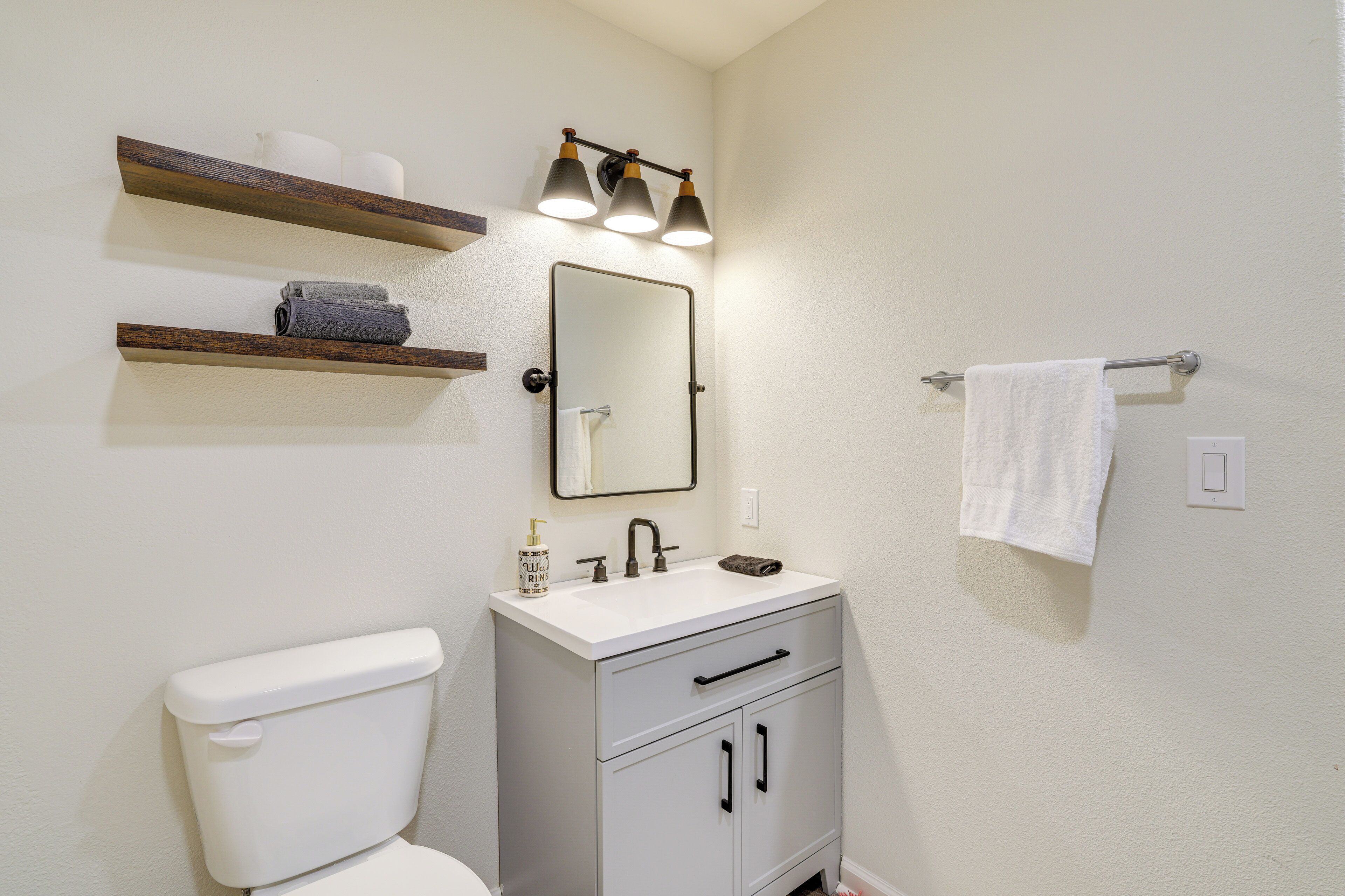 A bathroom with a toilet, sink, mirror, towel rack, and shelves with towels.