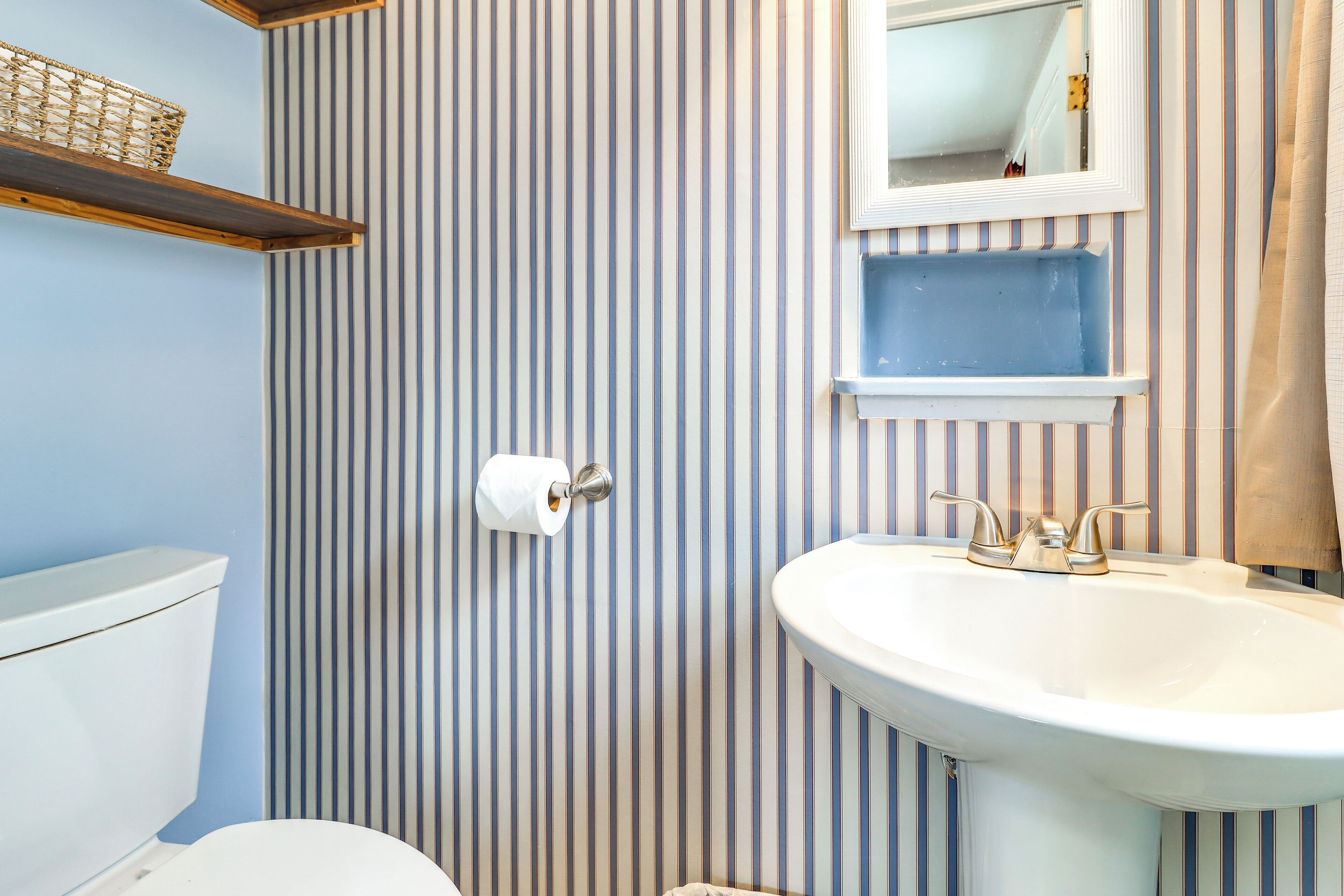 A bathroom with striped wallpaper, a white sink, a toilet, and a mirror above the sink.