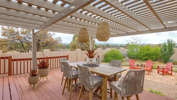 An outdoor patio with a pergola, wicker chairs, a table, and potted plants.