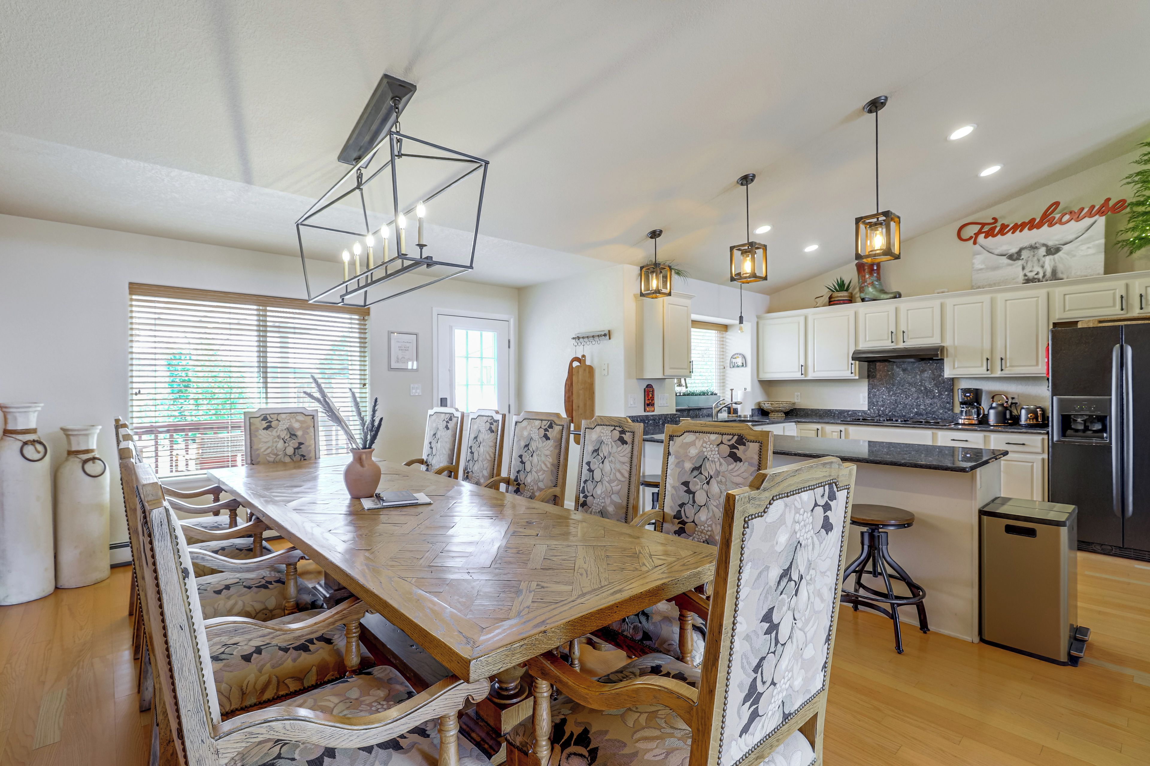 A spacious kitchen with modern appliances, a dining area with floral chairs, and a farmhouse sign on the wall.