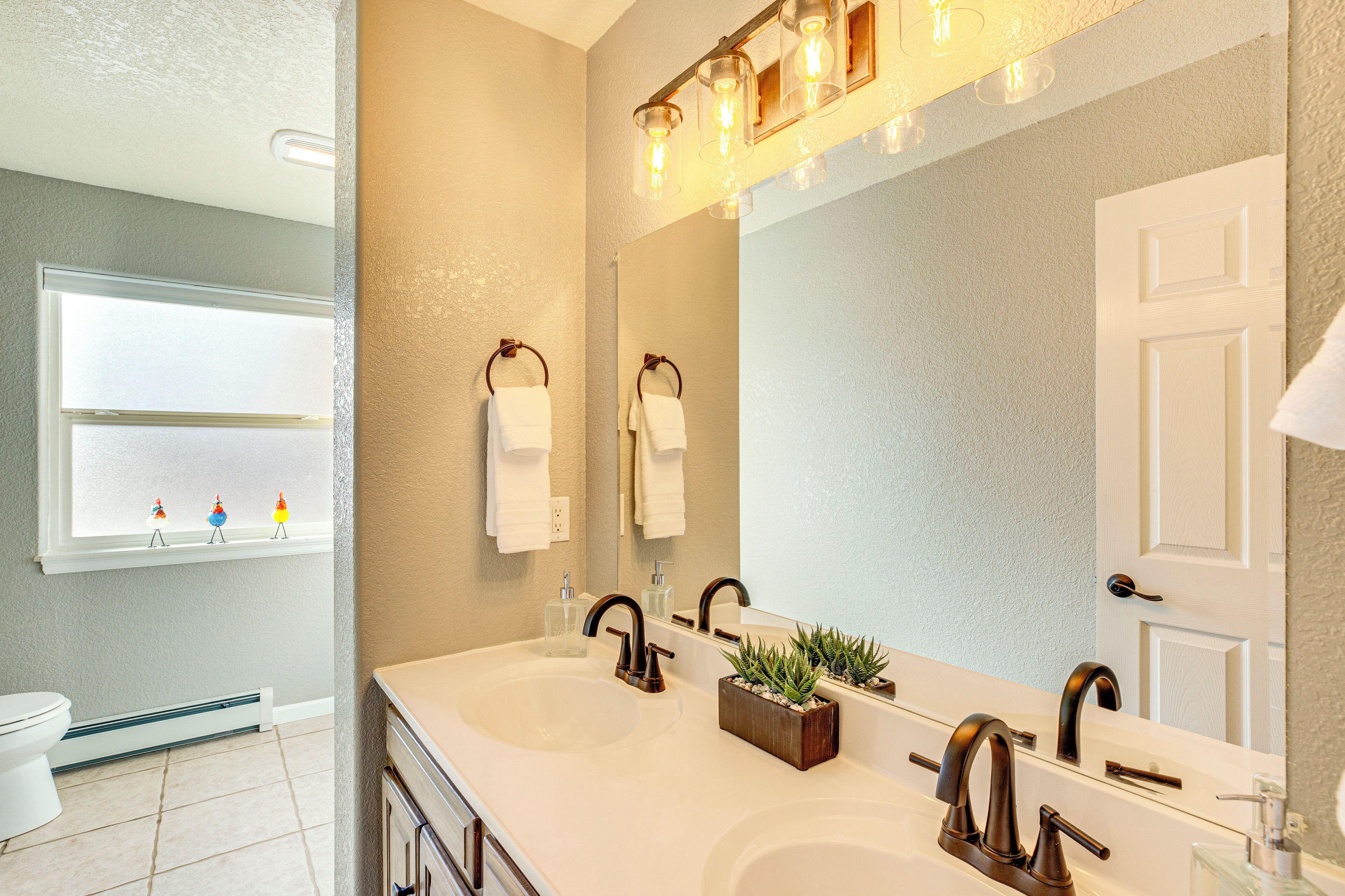 Een badkamer met een dubbele wastafel, een spiegel en een raam met decoratieve objecten.