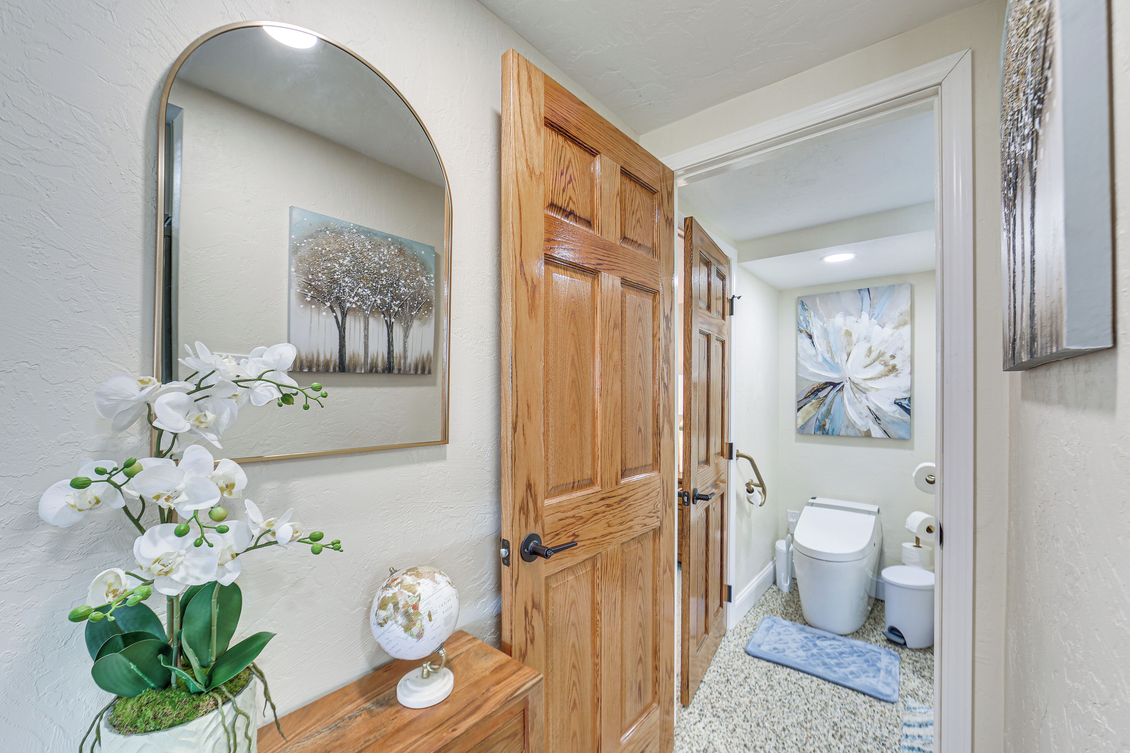 A bathroom with a wooden door, a globe on a wooden dresser, and a mirror on the wall.