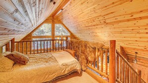 A cozy attic bedroom with a wooden ceiling, a large window, and a bed with patterned bedding. - Family-friendly Cabin w/ Fire Pit in Forest Lakes (Forest Lakes)