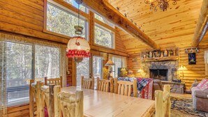 A wooden cabin interior with a dining table, chairs, a fireplace, and large windows. - Family-friendly Cabin w/ Fire Pit in Forest Lakes (Forest Lakes)