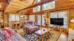 A log cabin interior with a cozy living room, wooden furniture, and large windows. - Family-friendly Cabin w/ Fire Pit in Forest Lakes (Forest Lakes)