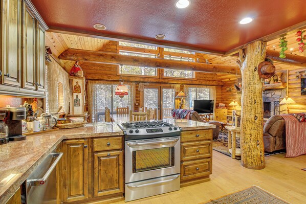 A spacious kitchen with wooden cabinets, a large island with a stove, and a stone fireplace.