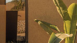 A modern building with a textured facade, a doorway leading to a garden, and large banana leaves in the foreground. - Silence Villas (Fethiye)