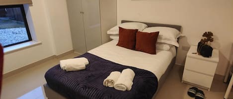 Quarto de hotel com cama, mesa de cabeceira, janela e um quadro na parede.