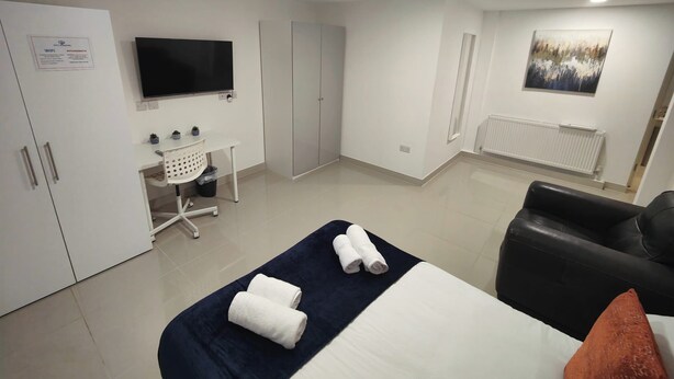 Quarto de hotel com cama, escrivaninha, televisão, guarda-roupa e radiador.