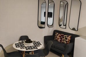 Una sala de estar moderna con una mesa de comedor redonda, sillas negras, un sofá gris con cojines estampados y tres espejos colgados en la pared.