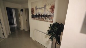Um corredor com um radiador, um vaso de plantas e uma pintura de uma ponte.