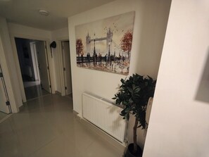 Un couloir avec un radiateur, une plante en pot et un tableau représentant un pont.