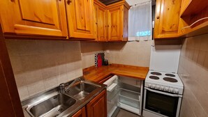 A kitchen with wooden cabinets, a stainless steel sink, a white stove, and a window with a white curtain. - Nature & Ski Retreat in Bad Kleinkirchheim (Bad Kleinkirchheim)
