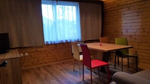 A room with wooden walls, a wooden table with chairs, a television, and a window with curtains. - Nature & Ski Retreat in Bad Kleinkirchheim (Bad Kleinkirchheim)