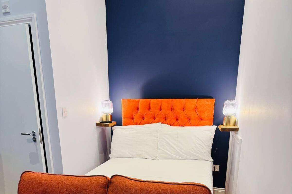 A room with a bed, orange upholstered sofa, and two bedside lamps.