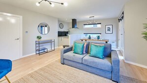 A modern living room with a grey sofa, a small side table, a mirror, and a kitchen in the background. - Host Stay Ropewalks Quarters VI (Liverpool)