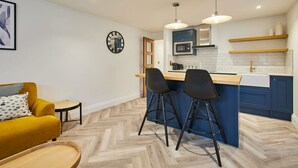 Een moderne keuken met een centraal eiland, barstoelen en een zithoek met een gele bank.