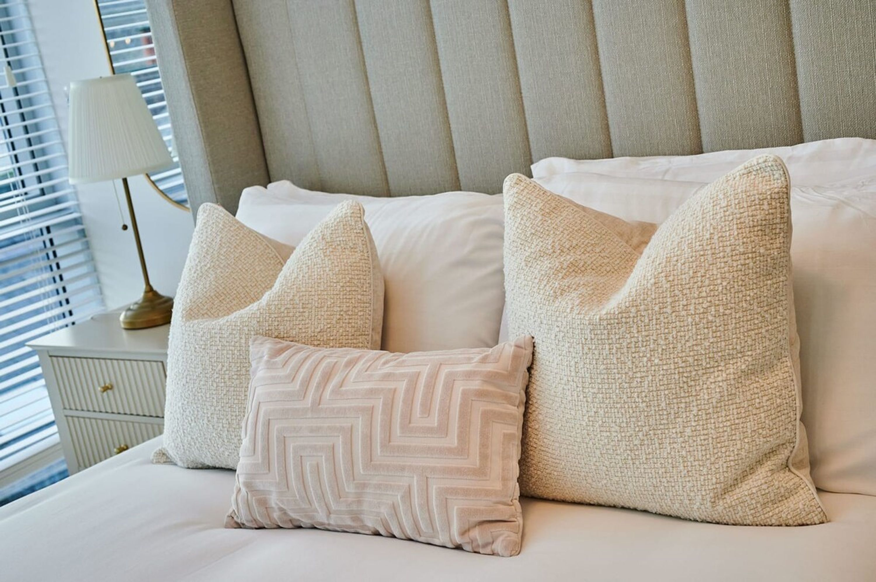 Una cama bien hecha con tres almohadas, una lámpara de noche y una mesita de noche.
