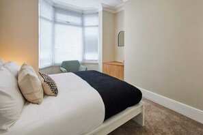 A bedroom with a bed, a chair, a small wooden table, and a window with blinds. - Host Stay Norton House (Stockton-on-Tees)