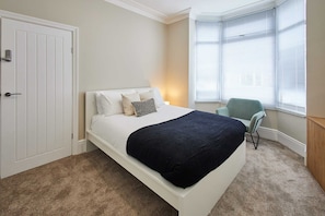 A bedroom with a bed, a chair, a window with blinds, and a door. - Host Stay Norton House (Stockton-on-Tees)