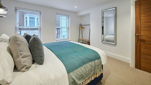 A bedroom with a bed, two windows, a mirror, and a wooden door. - Host Stay Sea Salt Apartment (Whitby)