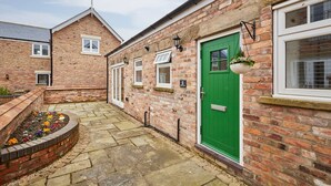 A brick building with a green door, numbered 5, and a small garden area with colorful flowers. - Host Stay Jubilee Close (Filey)