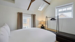 A bedroom with a large bed, a window with curtains, a bedside table with a lamp, and a coat rack. - Host Stay Jubilee Close (Filey)