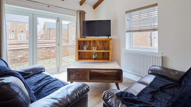A living room with leather sofas, a wooden coffee table, a TV on a stand, and a window with blinds. - Host Stay Jubilee Close (Filey)