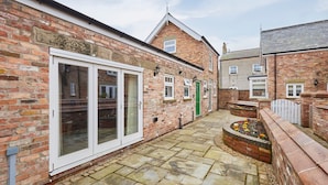 A courtyard with a brick building, a white-framed glass door, and a flower bed. - Host Stay Jubilee Close (Filey)