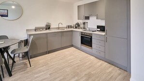 A modern kitchen with grey cabinets, a stainless steel sink, and a dining area with a round table and two chairs. - Host Stay 23 Waterside Place (Taunton)